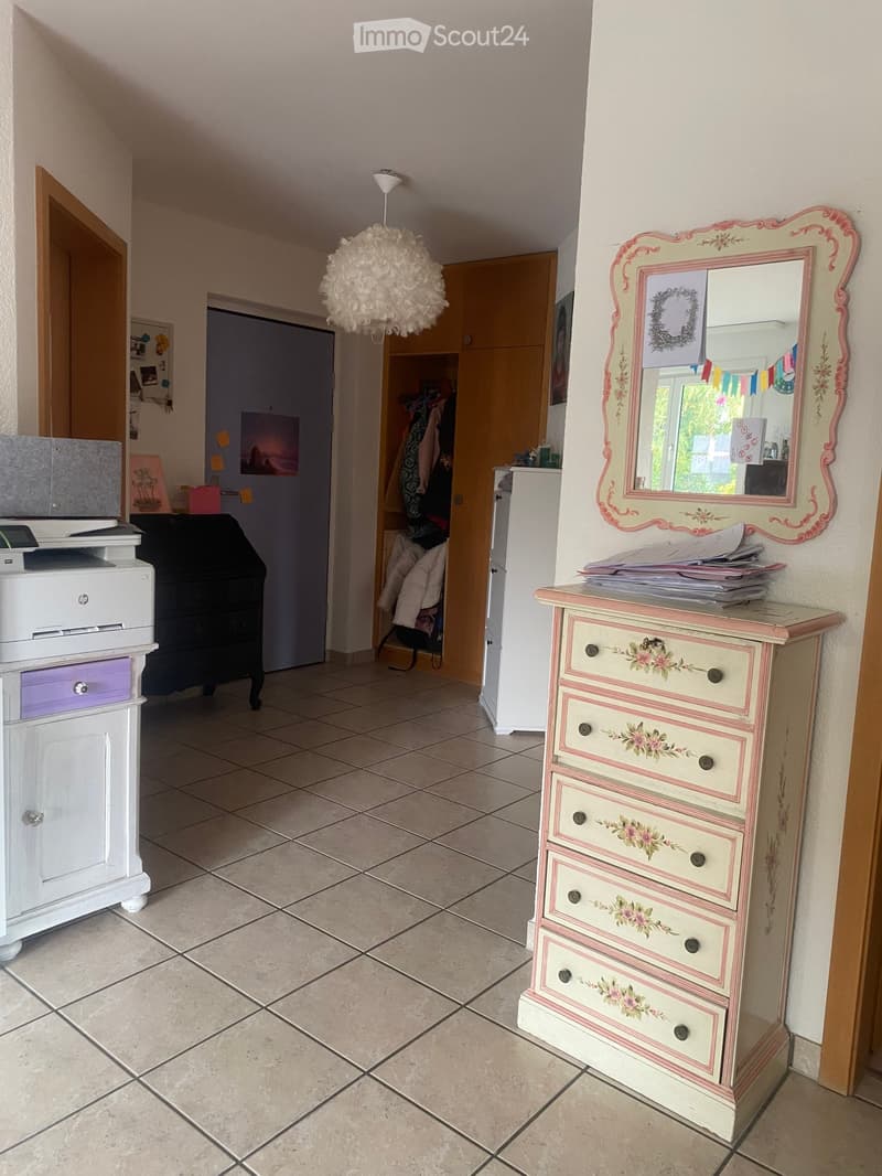A hallway with tiled flooring, a white cabinet, a floral-patterned dresser, a mirror, and a hanging ball lamp.