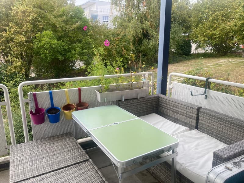 Balcony with a green table, wicker sofa, and hanging flower pots.