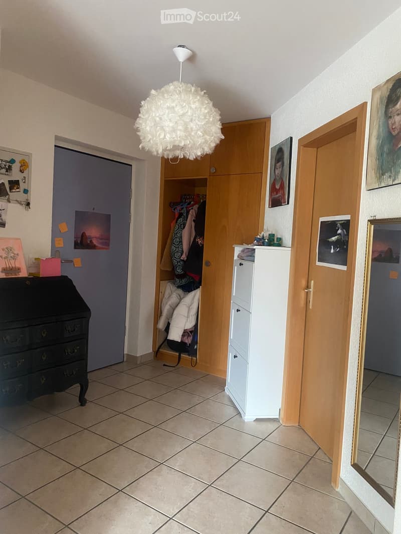 A hallway with a tiled floor, a hanging lamp, a wardrobe, a dresser, and several picture frames on the walls.