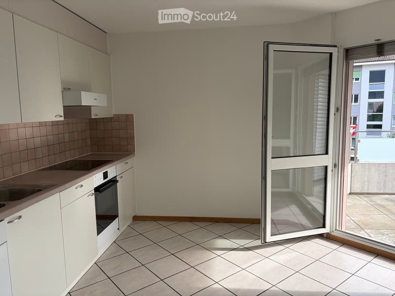 Modern kitchen with white cabinets, tiled backsplash, and a sliding glass door leading to a balcony.