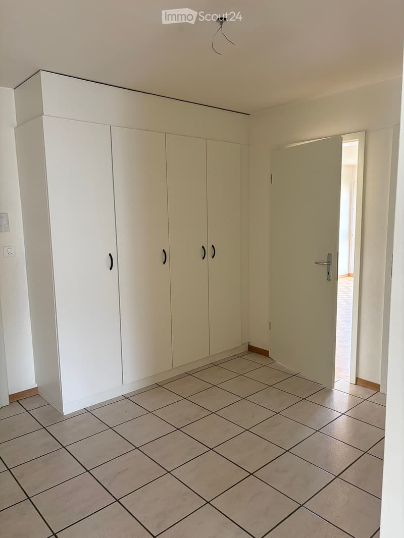 Empty room with tiled floor, white walls, built-in white closet, and an open doorway leading to another room.