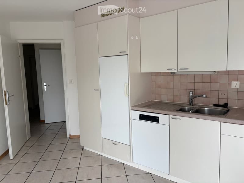 Modern kitchen with white cabinets, a stainless steel sink, and a dishwasher. The floor is tiled, and there is an open doorway leading to another room.