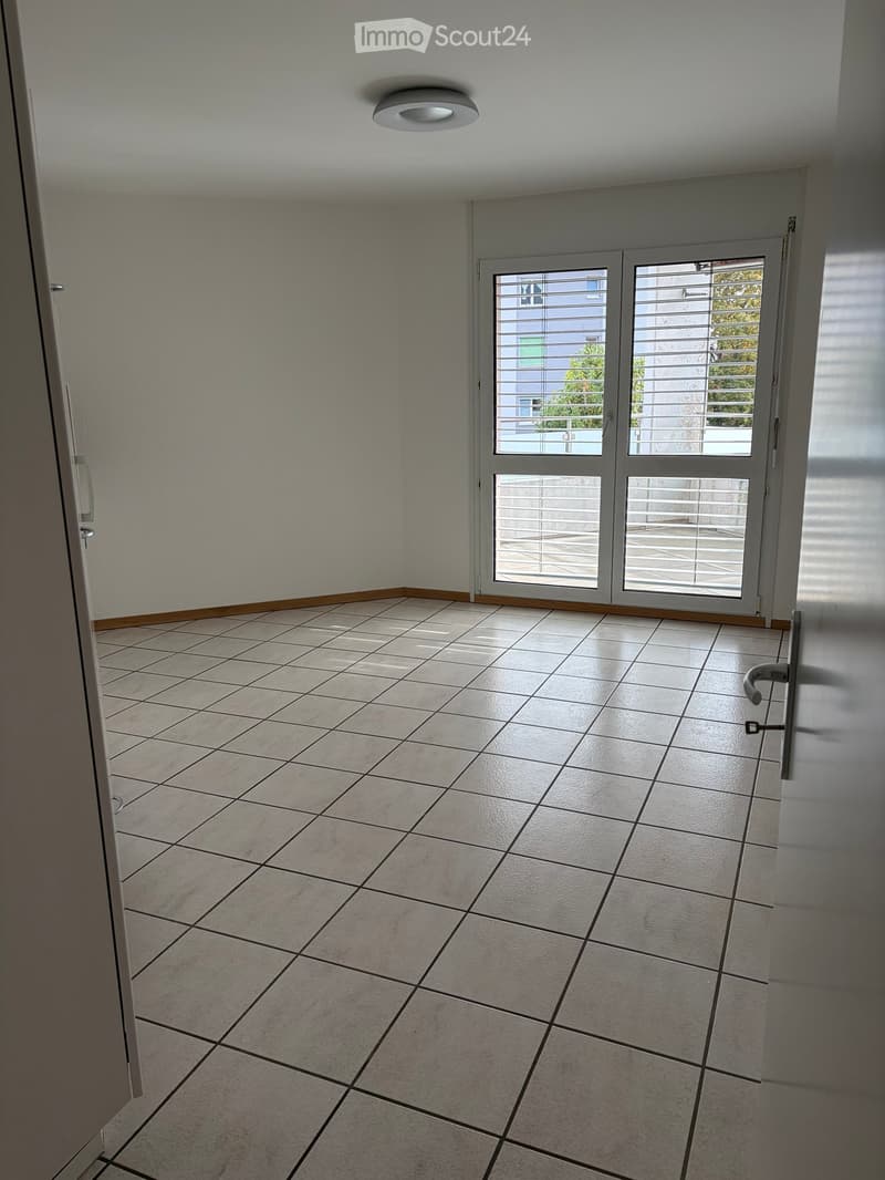 Empty room with tiled floor, white walls, and large sliding glass doors leading to a balcony.