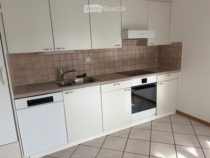 Modern kitchen with white cabinets, stainless steel sink, oven, and dishwasher. Brown tiled backsplash and beige tiled floor.