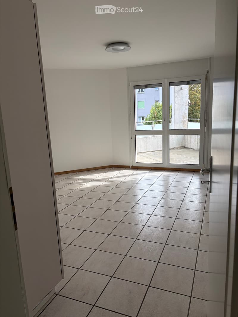 Empty room with tiled floor, white walls, and a large sliding glass door leading to a balcony.