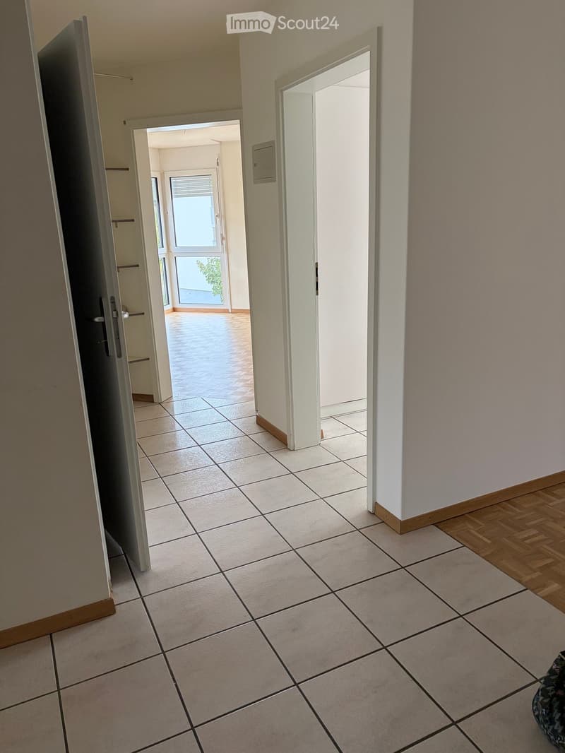 Empty hallway with tiled floor, white walls, and open doors leading to other rooms and an outdoor area.