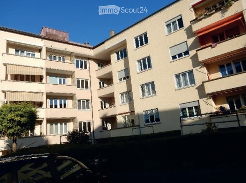 Multi-story residential building with multiple windows, balconies, and beige facade.