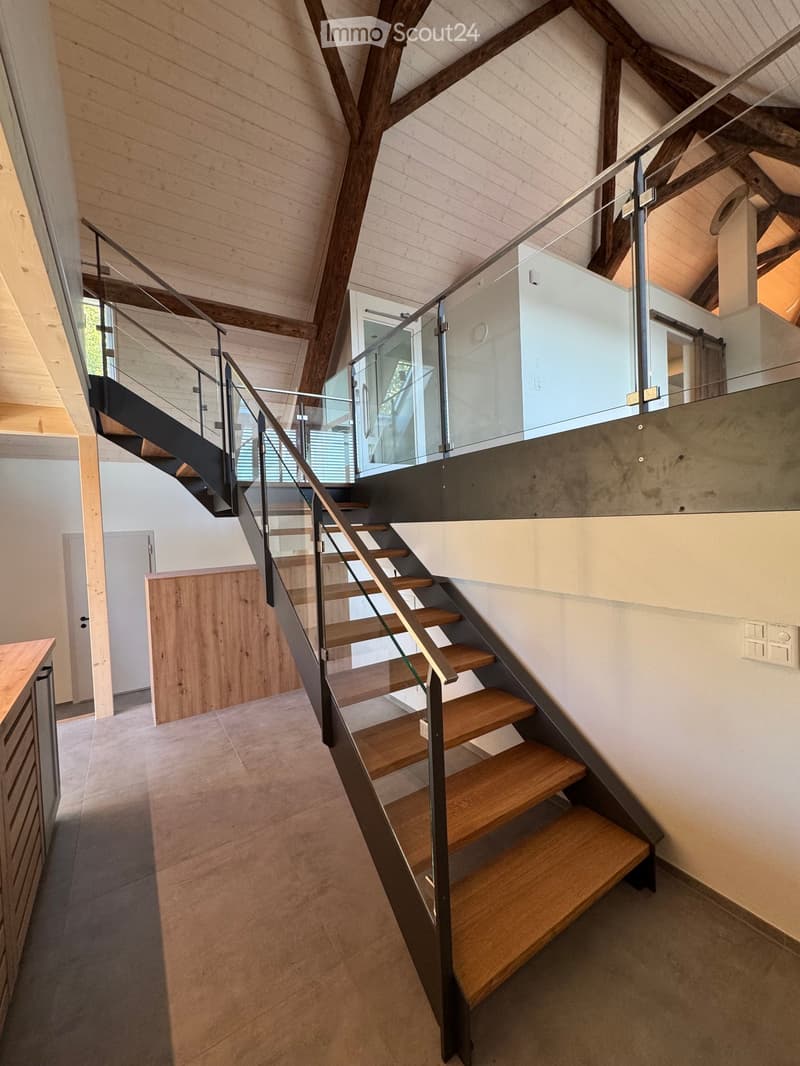 Modern staircase with wooden steps and metal railings, featuring a glass balustrade and exposed wooden beams in the ceiling.