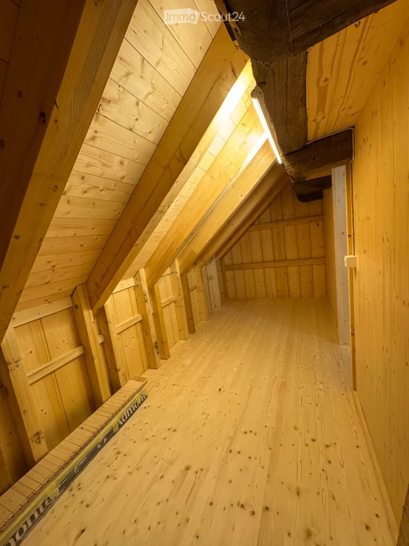 Empty wooden attic corridor with exposed wooden beams and slanted ceiling, natural lighting from the side.