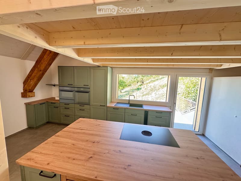 Modern kitchen with light green cabinets, stainless steel appliances, wooden island, and large windows overlooking a garden.
