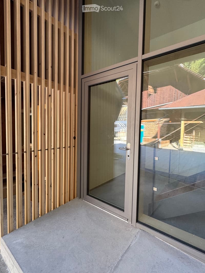 Modern balcony with large glass doors, concrete floor, and wooden slatted privacy screen.