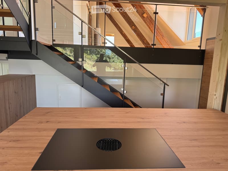 Modern interior with a wooden table, sleek staircase with glass railing, and exposed wooden beams on the ceiling.