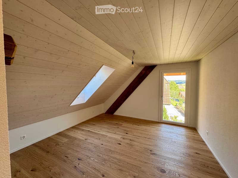 Empty attic room with wooden ceiling, wooden floor, skylight window, and sliding door leading outside.