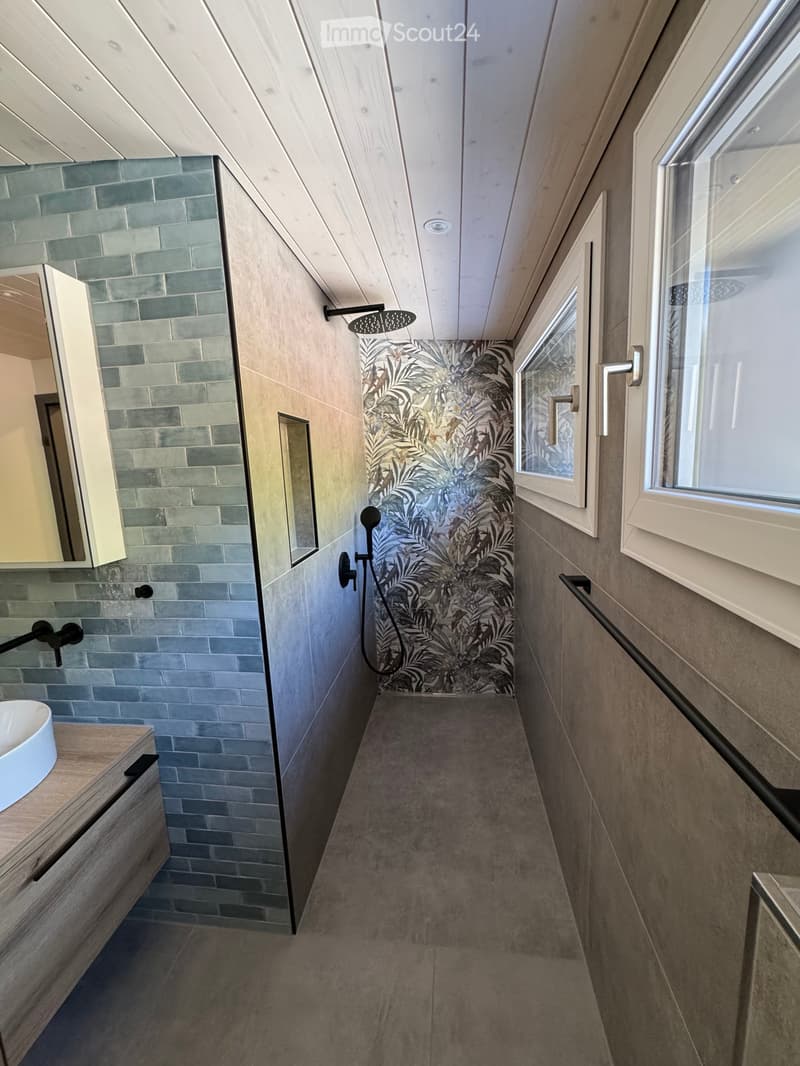 Modern bathroom with a sleek design, featuring a sink with a wooden vanity, a shower area with a glass enclosure, and a decorative wall with a leafy pattern.