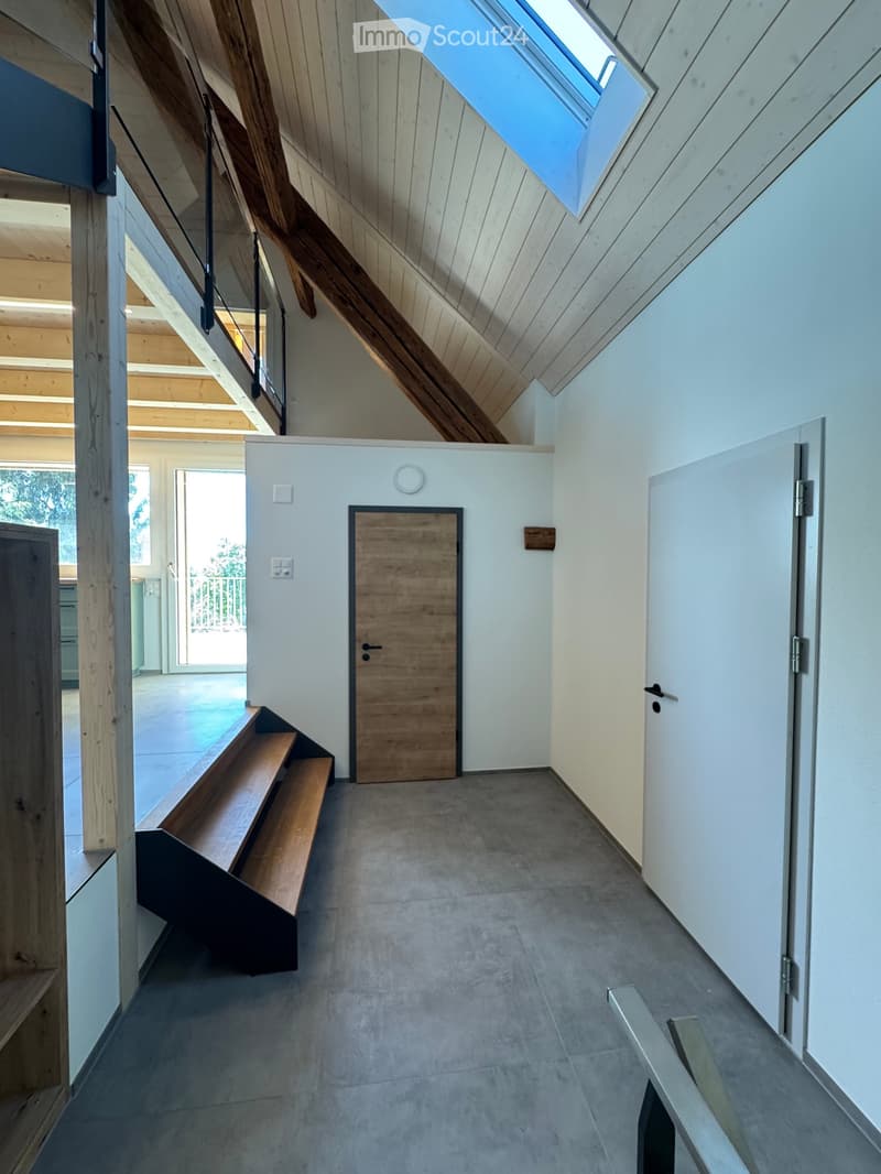 Modern hallway with wooden staircase, concrete floor, white walls, and a skylight at the top.