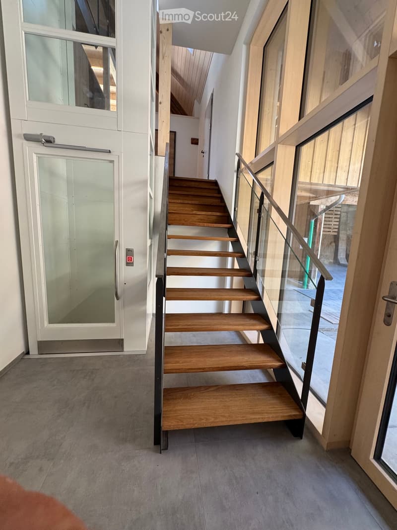 Modern hallway with wooden staircase, glass railing, and white doors.