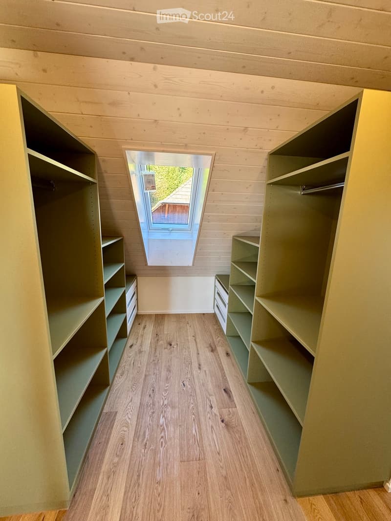 Empty hallway with wooden flooring, built-in shelves on both sides, and a skylight window at the end.