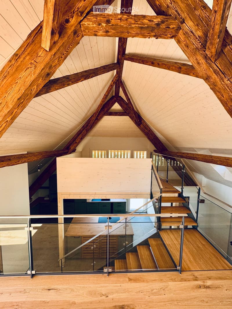 Open wooden staircase with glass railing, exposed wooden beams, and light-colored wooden flooring.