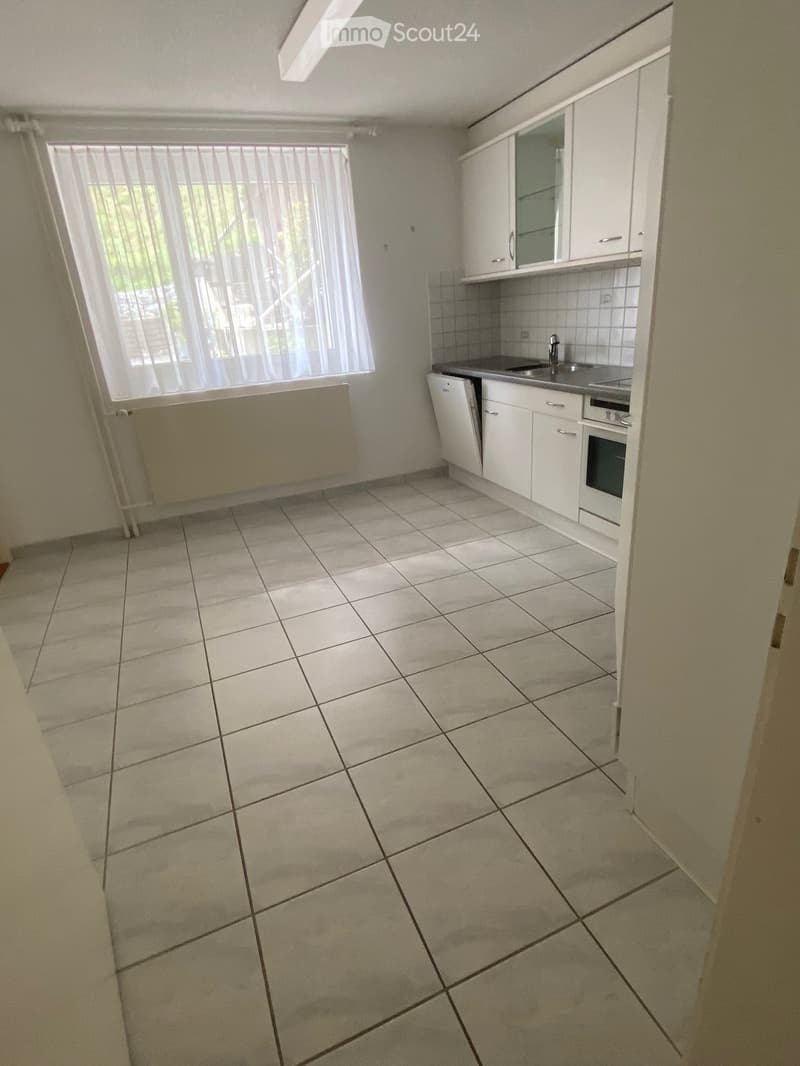 Empty kitchen with white cabinets, tiled floor, and a window with blinds. No appliances or furniture are present.