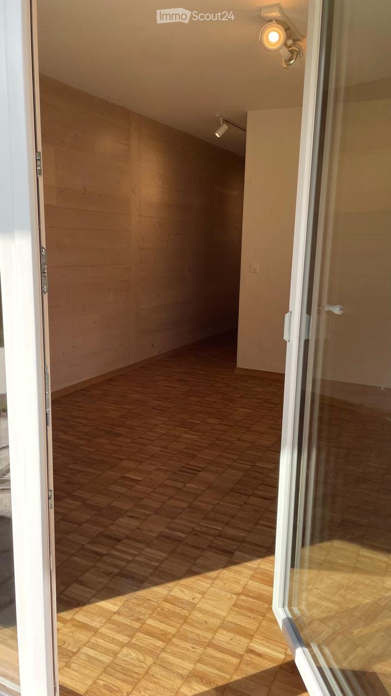 Empty hallway with wooden flooring, white walls, and recessed lighting. The space is well-lit with natural light coming from a large glass door at the end.