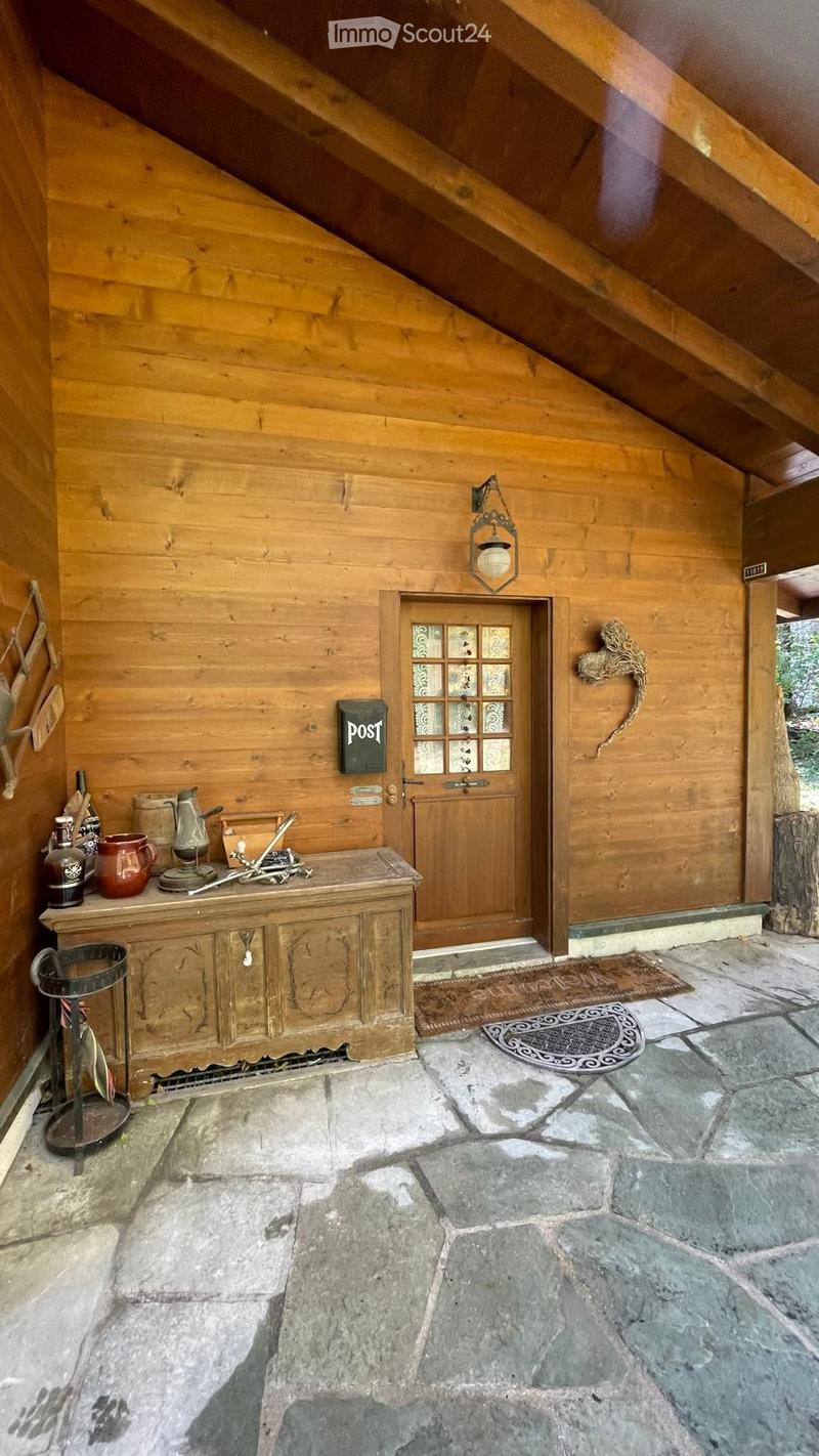 A wooden-furnished entryway with a stone floor, a small wooden table with decorative items, a hanging lantern, and a wooden door with glass panels.