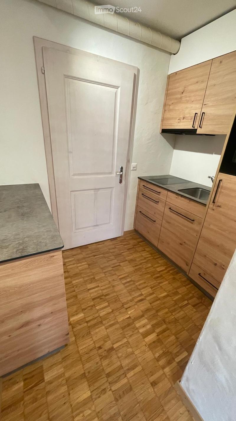 Modern kitchen with light wooden cabinets, a stainless steel sink, and a wooden countertop. The floor is made of light wooden planks, and there is a white door leading to another room.