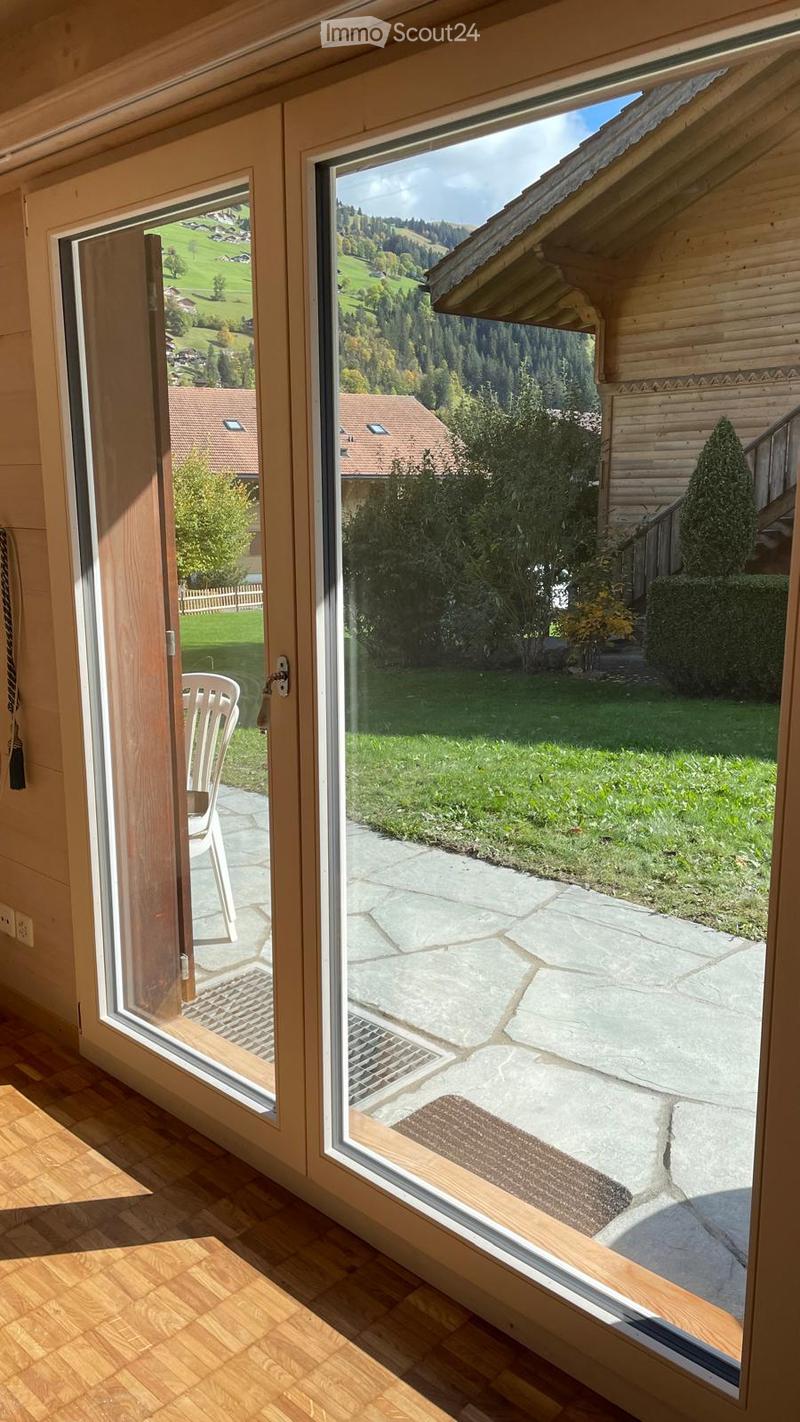 Large sliding glass doors open to a stone patio with a view of green hills and a distant village. A white plastic chair is visible near the entrance.