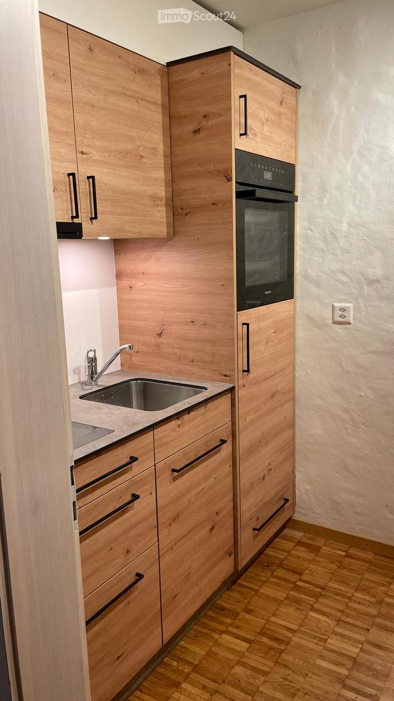 Modern kitchen with light wooden cabinets, stainless steel sink and faucet, built-in oven, and wooden flooring.