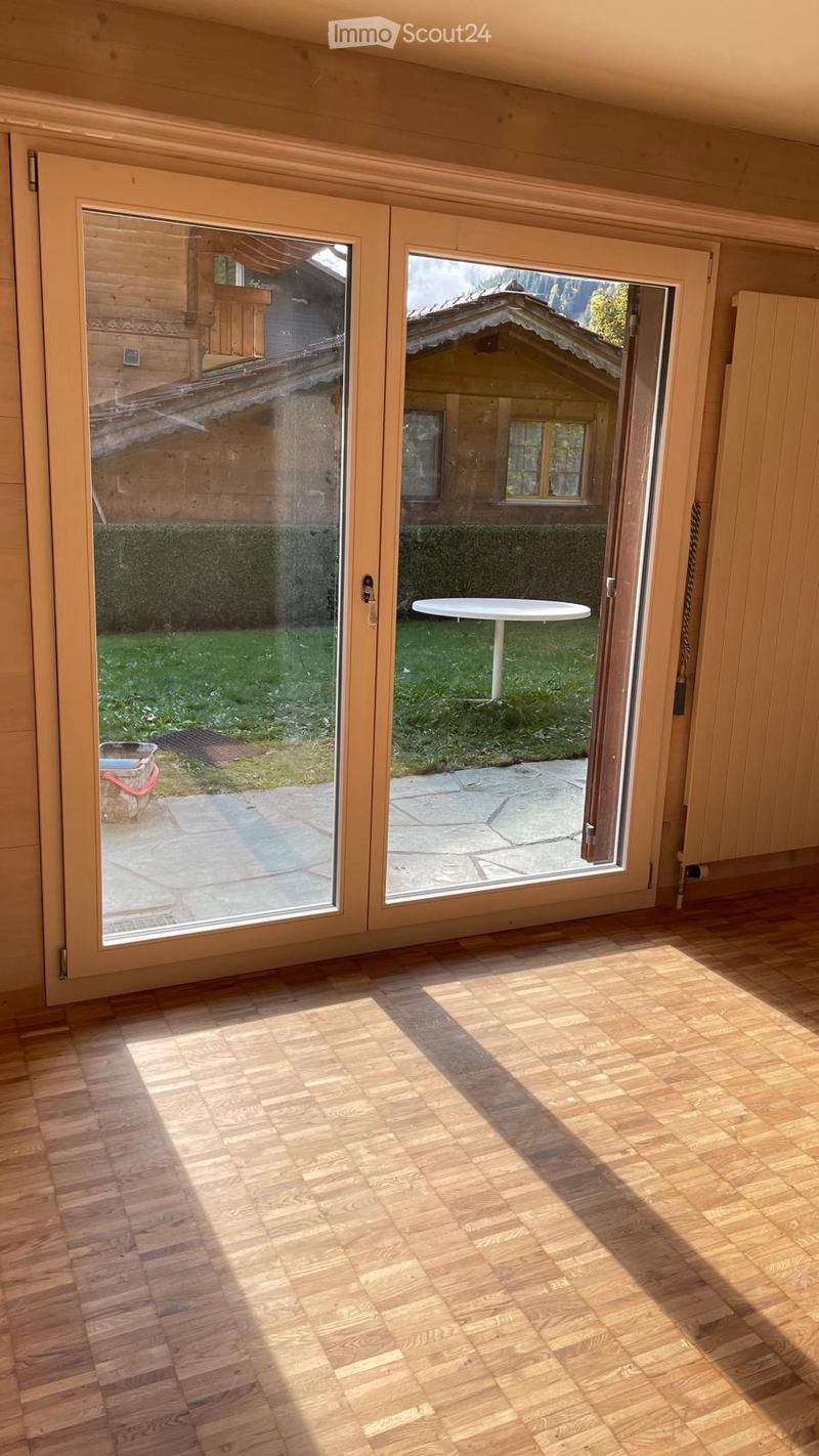 Empty room with wooden flooring and large sliding glass doors leading to a patio area with a small table and outdoor space.