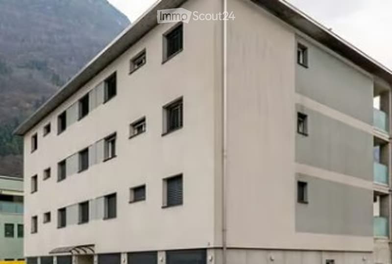 A multi-story residential building with a light beige facade and numerous windows, situated in a mountainous area.