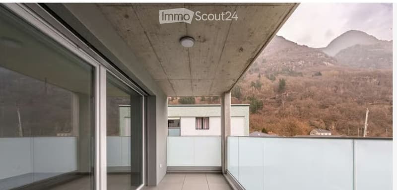 Modern balcony with large glass panels, concrete ceiling, and scenic mountain view.