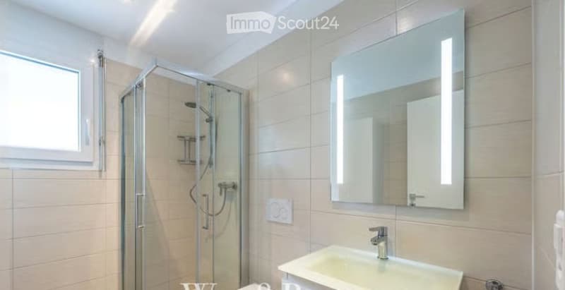Modern bathroom with a white tiled shower, a large illuminated mirror, and a white sink.