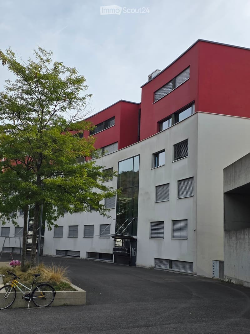 Modern two-story building with red and white facade, large windows, and a bicycle parked nearby.