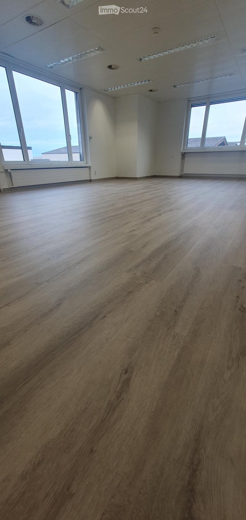 Empty room with wooden flooring, large windows, and white walls.
