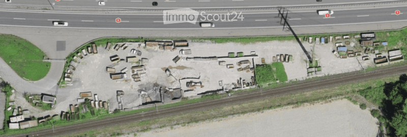 Aerial view of a construction site with scattered materials, partially built structures, and a nearby road and railway tracks.