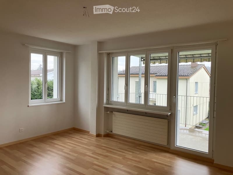 Empty room with wooden flooring, large windows, radiator, and a sliding glass door leading to a balcony.