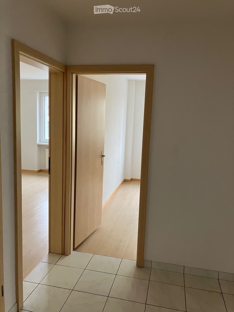 Empty hallway with tiled floor and wooden doors leading to other rooms.