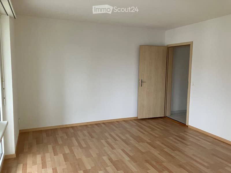 Empty room with light wooden flooring and white walls, featuring a single wooden door leading to another space.