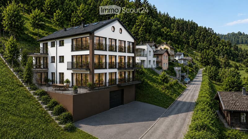 Modern two-story house with large windows and balconies, situated on a hillside with a scenic view of the surrounding forest and valley.