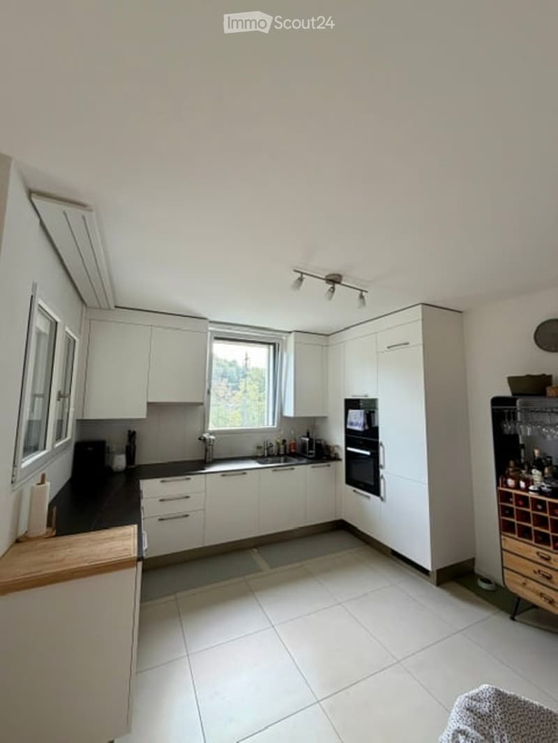 Modern kitchen with white cabinets, black countertops, and a built-in oven. Features a wine rack, a refrigerator, and a light fixture above the sink.