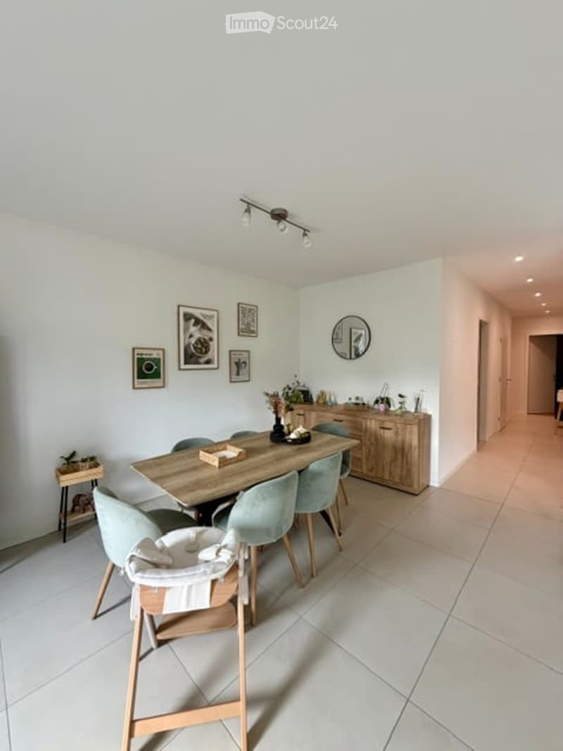 Bright dining area with a wooden dining table, four matching chairs, a baby chair, a side table, a wooden cabinet, a round mirror, and several framed pictures on the wall.