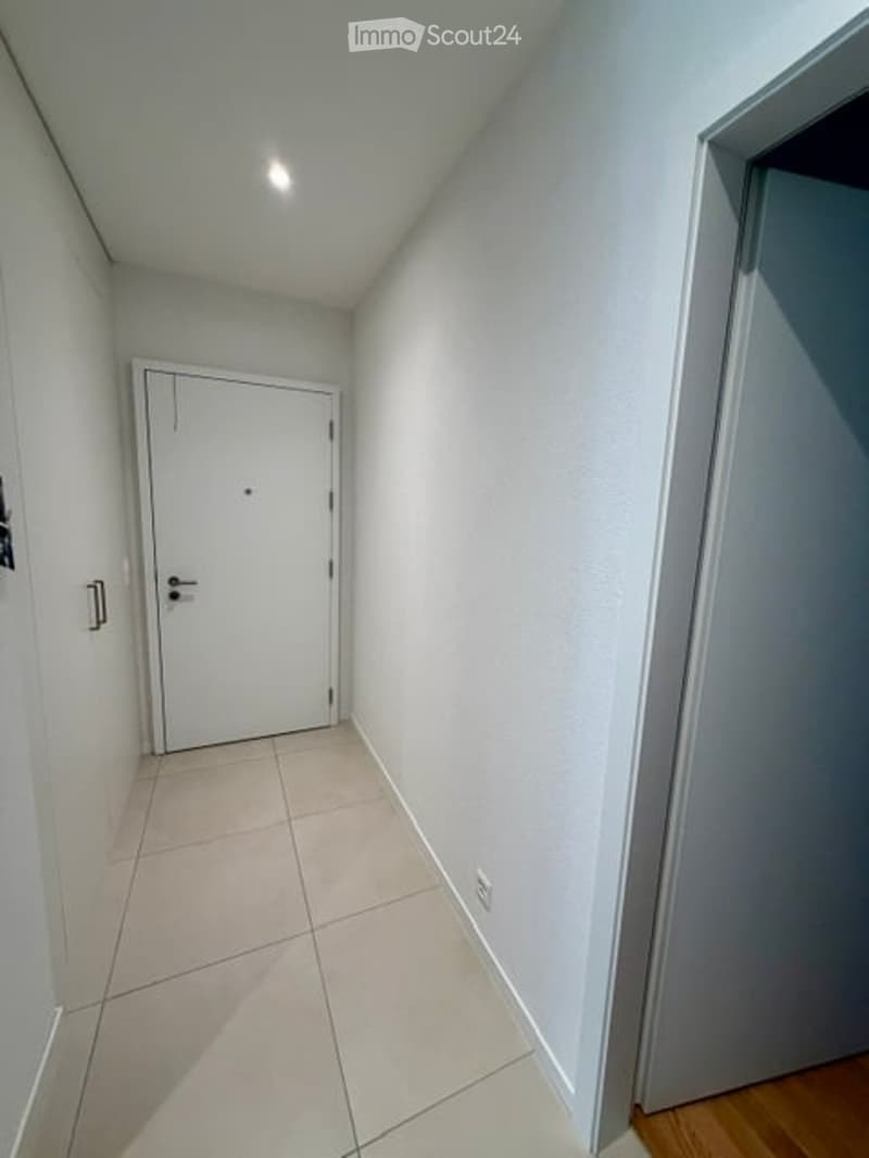 Empty hallway with white walls, tiled floor, and a closed white door at the end.