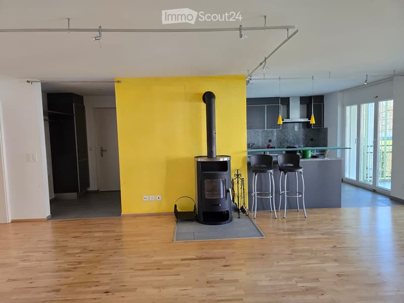 Open-plan living and kitchen area with wooden flooring, a modern fireplace, and a kitchen counter with stools.