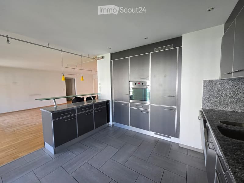 Modern kitchen with grey cabinets, stainless steel oven, granite countertops, and a glass table with stools.