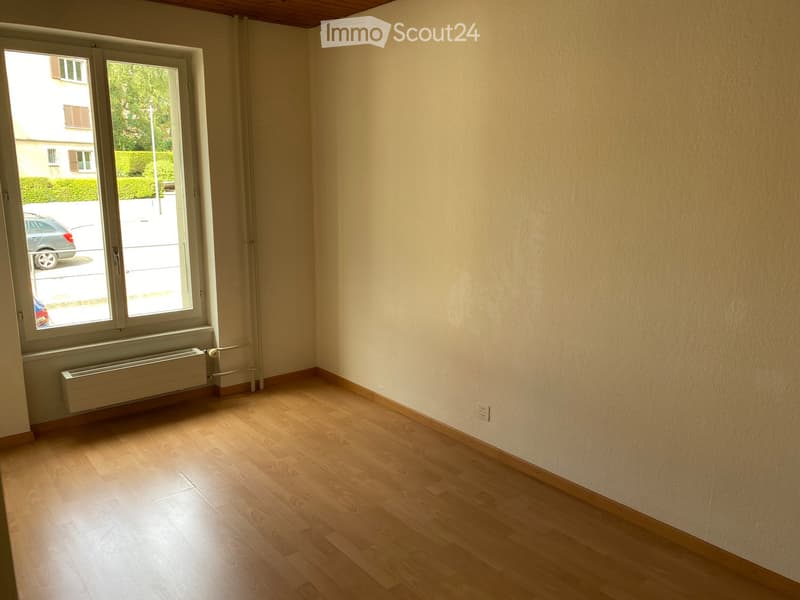 Empty room with wooden flooring, light-colored walls, and a large window with a radiator below it.