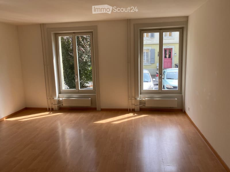 Empty room with wooden flooring, large windows, radiators, and natural light. No furniture or furnishings present.