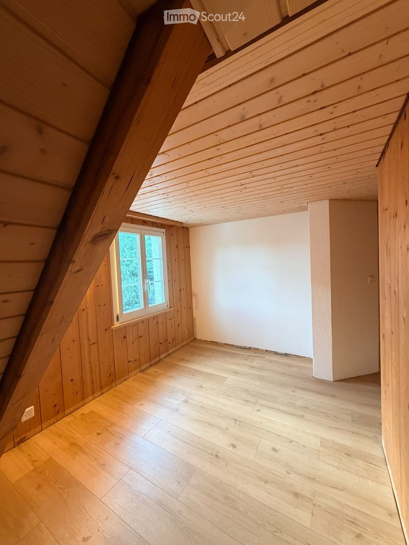 Empty attic room with wooden walls, wooden floor, and a small window letting in natural light.