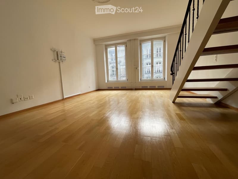 Empty room with wooden flooring, large windows, and a staircase leading upwards.