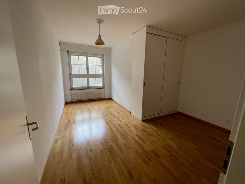 Empty room with wooden flooring, white walls, a large window, a built-in closet, and a hanging light fixture.