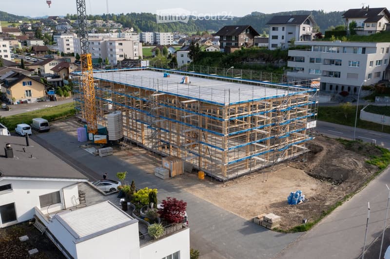 A multi-story building under construction with scaffolding, surrounded by other residential buildings and a crane in the background.